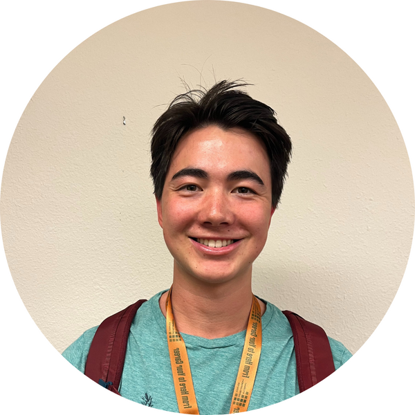 Close-up headshot of tutor Wyatt wearing a backpack and green shirt, standing in front of a white wall.